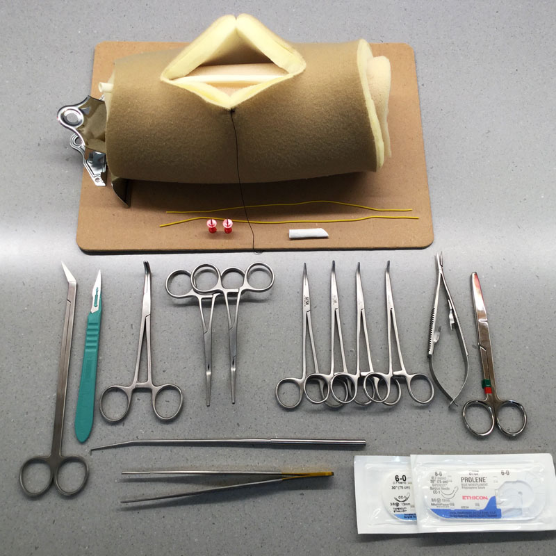Set-up for a vascular surgery anastomosis simulation including a large foam roll, scalpels, clamps, and other surgical tools.