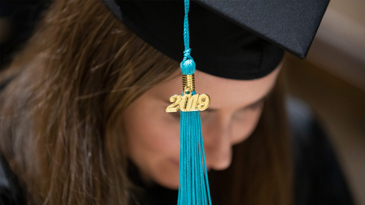 Graduate wearing a cap and gown, her blue 2019 tassle in sharp focus