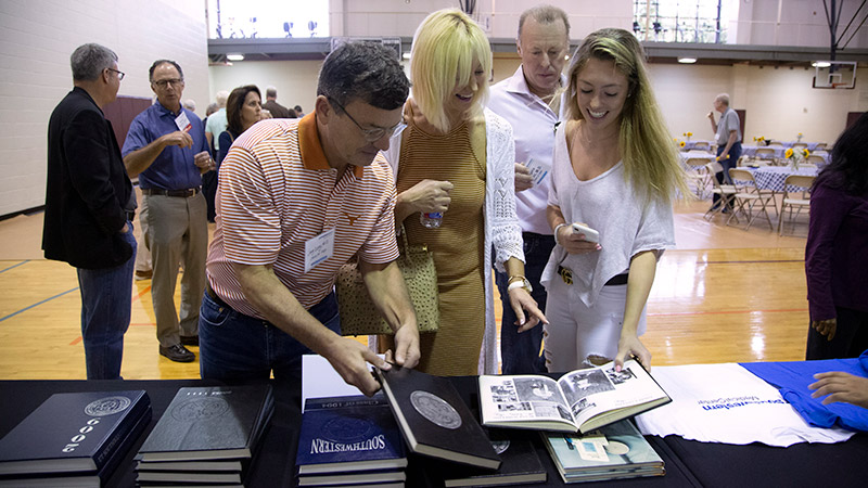 Four people flipping through stacks of yearbooks on a table