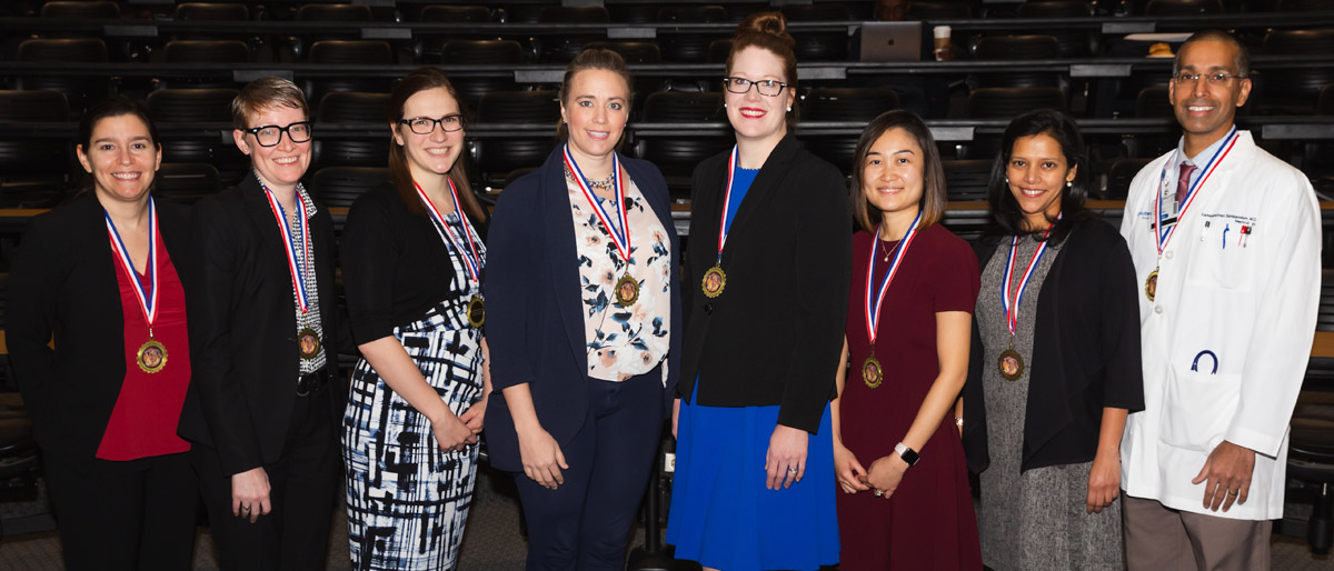 Eight people smiling, wearing medals