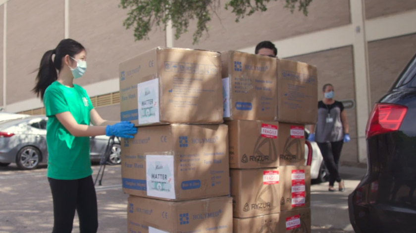 Girl in green shirt and mask standing by stack of boxes