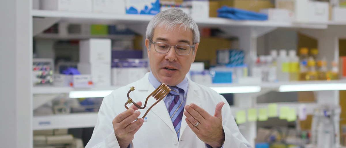 A man with gray hair examines a piece of curled copper tubing.