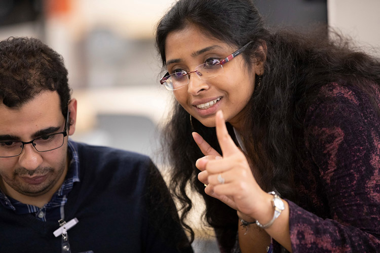 Woman standing next to man sitting at computer