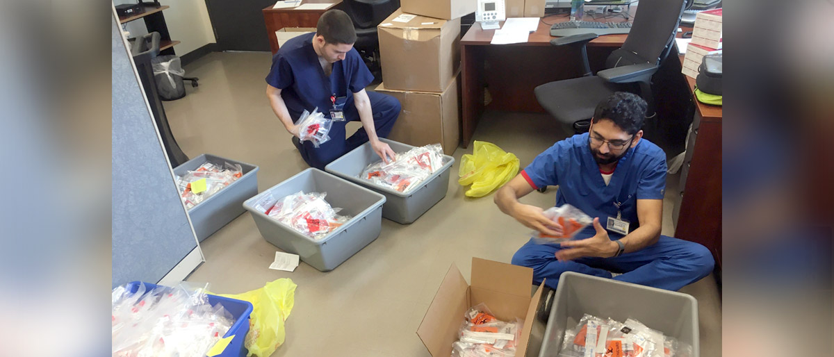 Two men in scrubs sorting medical test kits into boxes