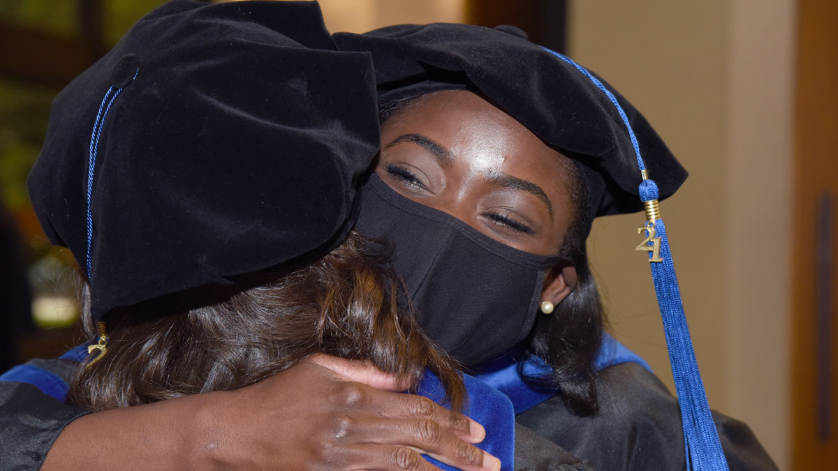 Woman in graduation gown hugging another in the same attire