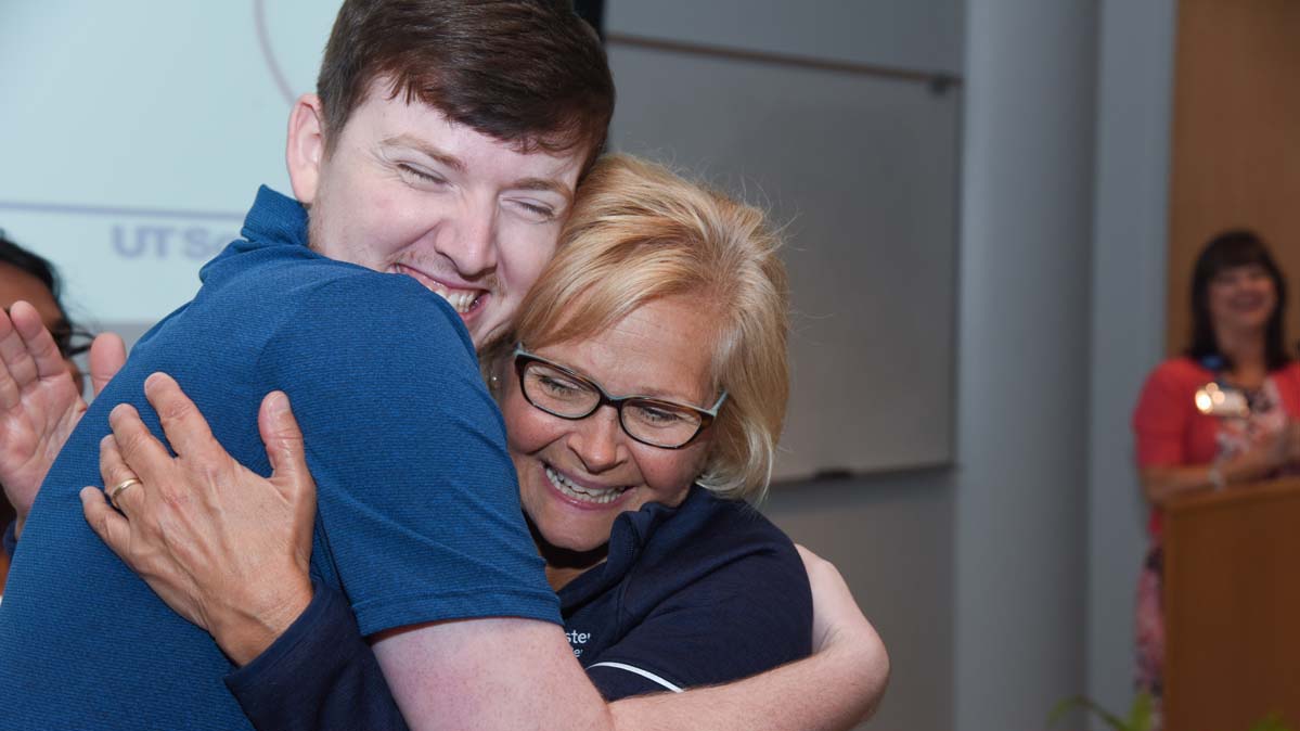 Newly graduated nurse hugging educator at commencement ceremony