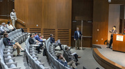 At the podium, David Tsen, M.D., Ph.D., Assistant Professor of Biomedical Engineering, talks about his work to develop surface-scanning visible and near-infrared ultrashort pulsated (USP) laser devices that can inactivate viruses, bacteria, fungi, and mycoplasma while limiting damage to cells, blood proteins, and vaccine antigens. This effort could lead to potential application of USP laser devices in prevention and therapy of infectious diseases and production of new vaccines.