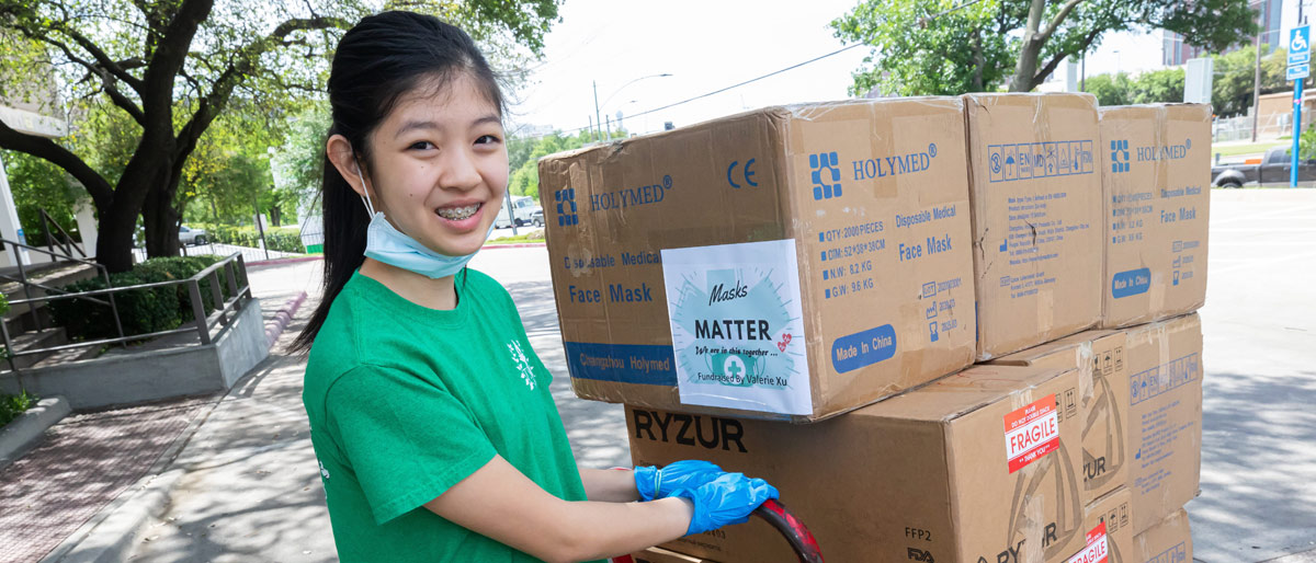 Young girl with mask smiling while pulling cart of boxes