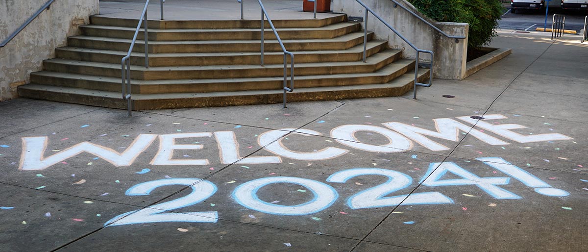 Stairwell entry to buildling, with Welcome 2024 written in chalk