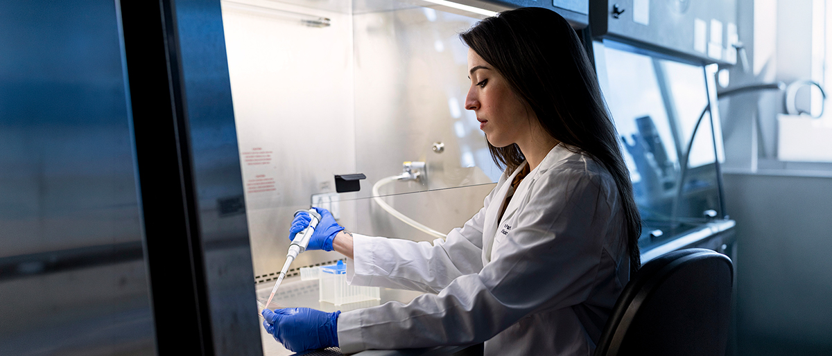 Woman at a desk, in a lab, using a dropper.