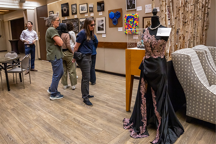 5 people look at art in gallery area including an embroidered evening gown on a mannequin in the left foreground