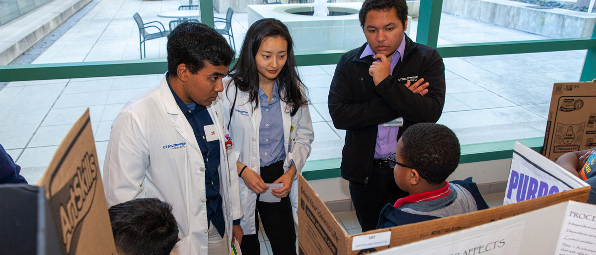 Three people talking in lab coats talking to child in front of poster