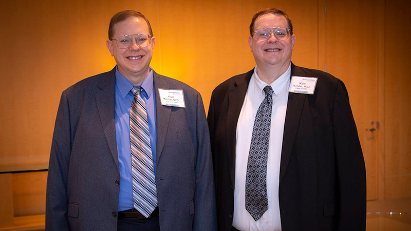 Two men standing next to each other smiling, and have a very similar appearance