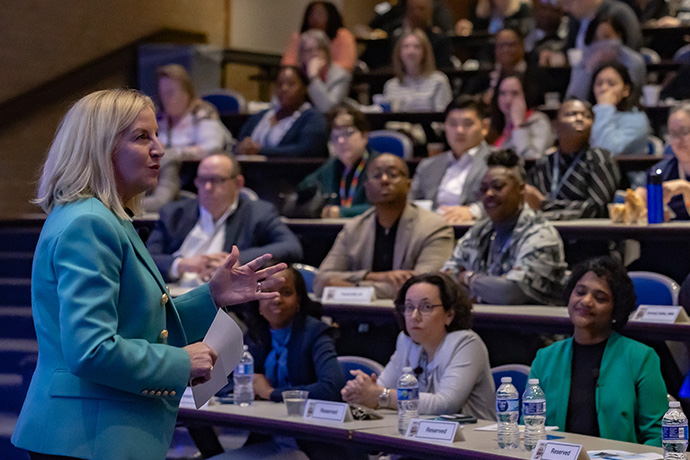 Susan Hernandez, blonde hair with blue blazer, addresses audience at Women's History event