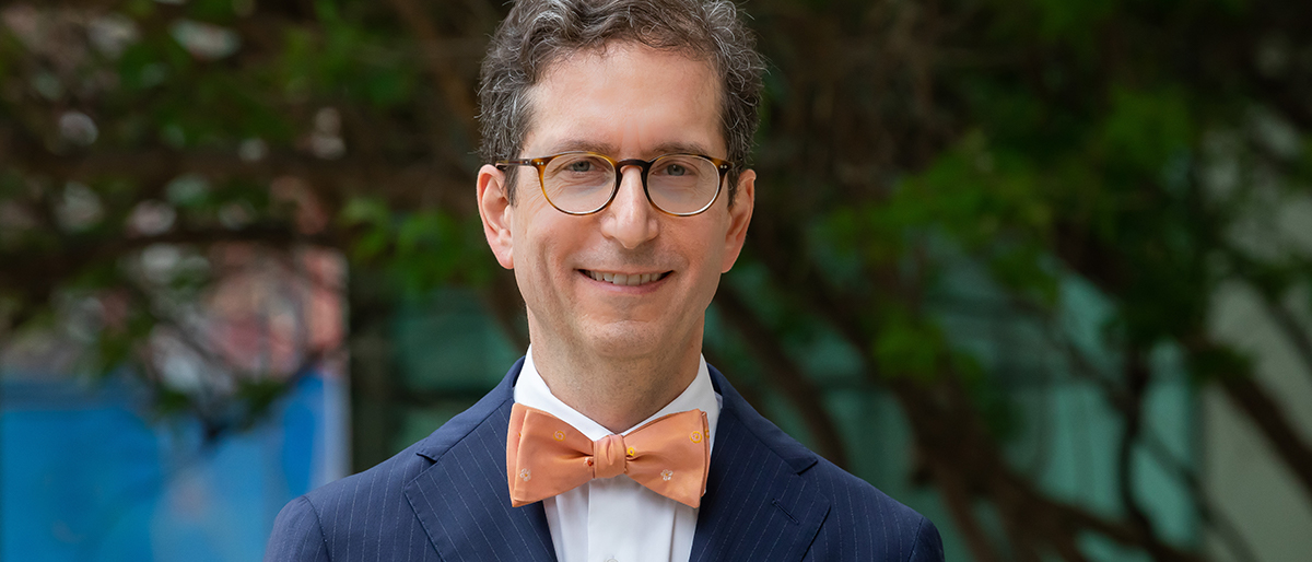 A man with glasses, blue suit, and a orange bowtie