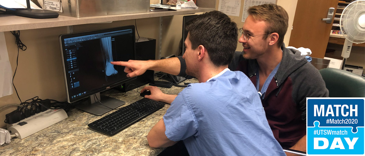 Two men, one in scrubs, sitting at a computer desk and looking at an x-ray