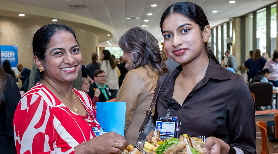 2 dark haired women stand at buffet with crowd behind them