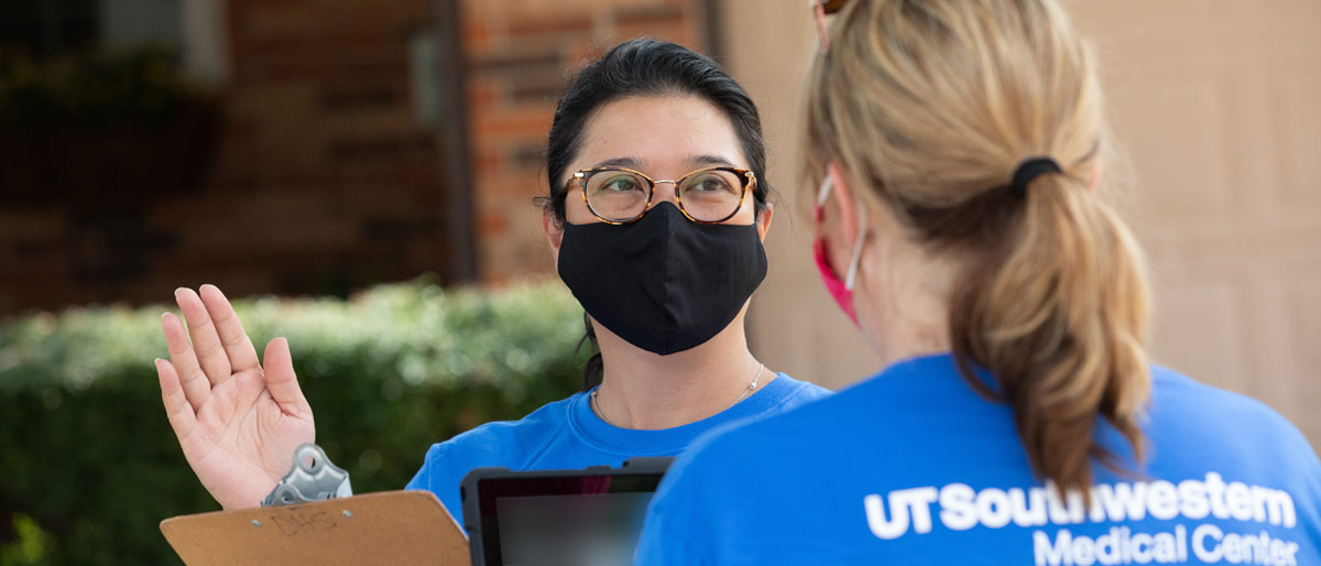 Woman in mask holding clipboard talking to person in UTSW shirt