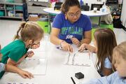 Teacher Jennifer Mayen helps a group of students learn and write alphabet letters.