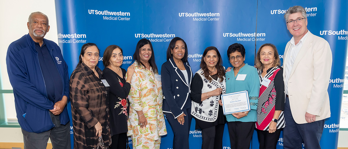 A group of men and women stand with a smiling woman holding up a certificate.