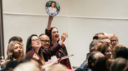 An enthusiastic graduate supporter holds up an image of her loved one and cheers as the student receives her degree.