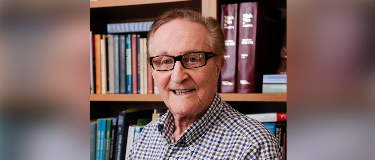 Man wearing glasses and a checkered shirt in front of a bookcase