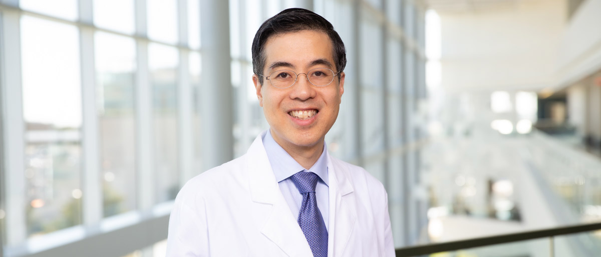 Man with dark hair, glasses wearing a white lab coat