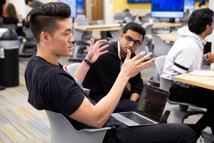 Young man sitting with laptop in lap, talking to team