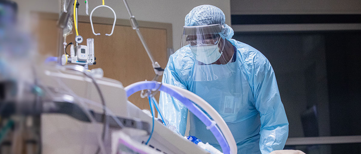 Man in scrubs and mask at hospital bed