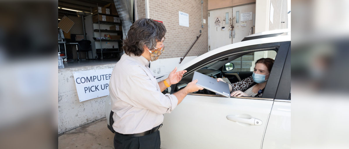 Man in mask handing laptop to masked woman in car