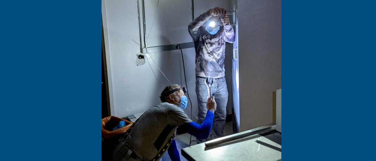 Two men in masks and headlamps working with tools