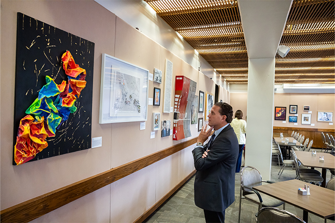dark-haired man in blue suit inspects colorful artwork on gallery wall