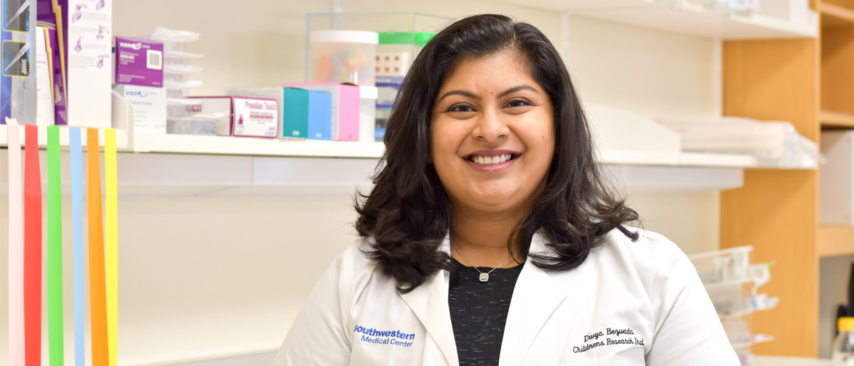 Woman in white lab coat and black shirt, standing in lab