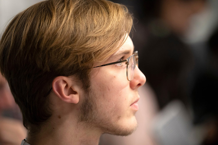 Man with glasses and dirty blonde hair looking off in the distance