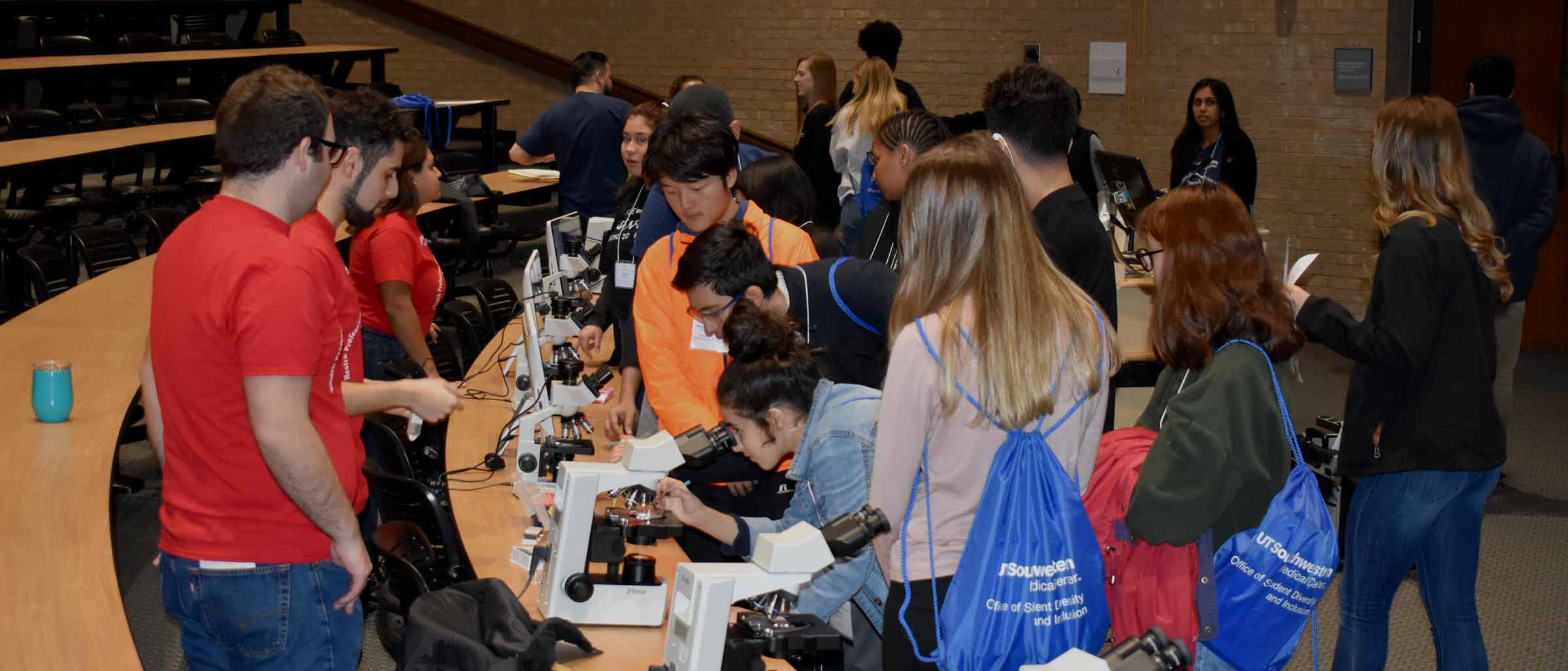 Crowd of teenagers looking into microscopes