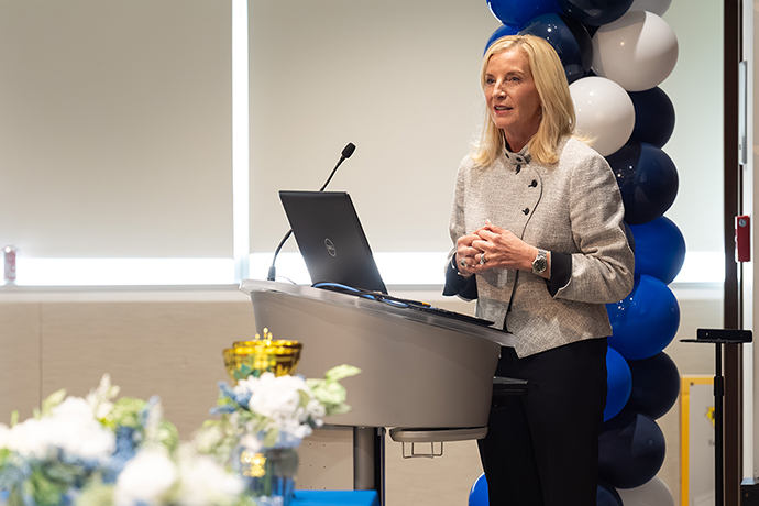 Woman standing in front of a column of balloons speaks from a podium.