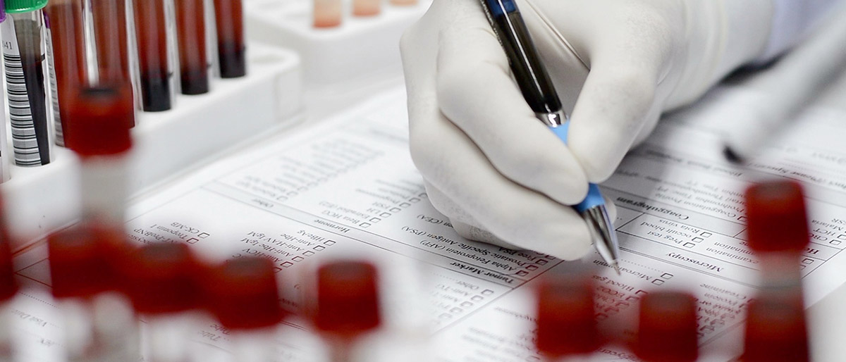 Gloved hand writing while surrounded by tubes of blood samples