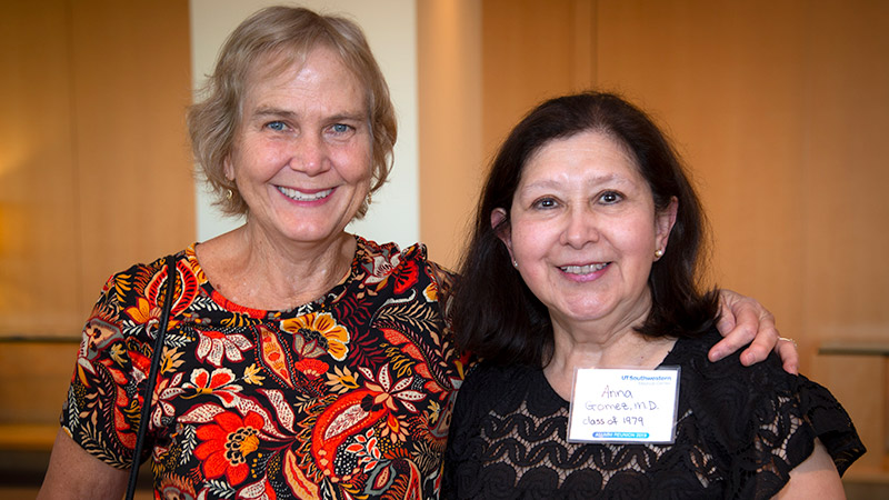 Two women standing next to each other and smiling, one with her arm around the other's shoulder