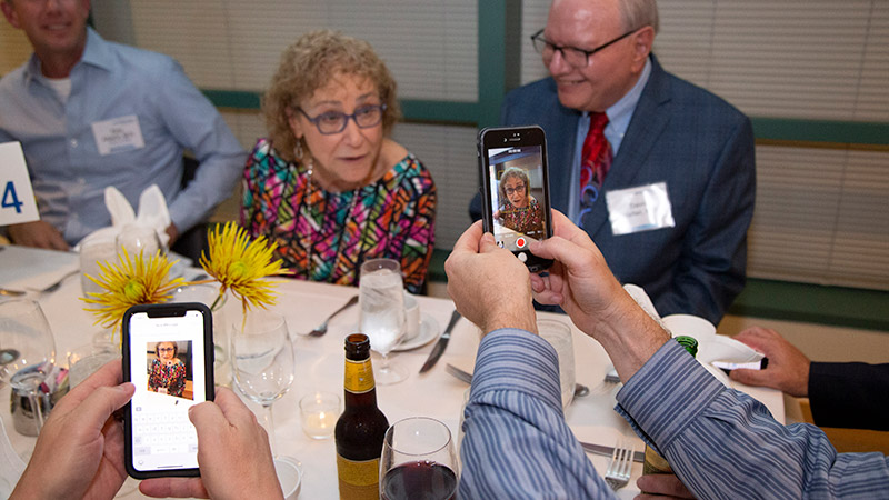 Two people recording video of a woman seated at a table.