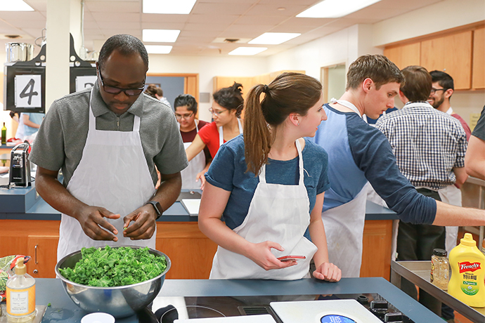 Apron-clad people preparing food in a large kitchen.