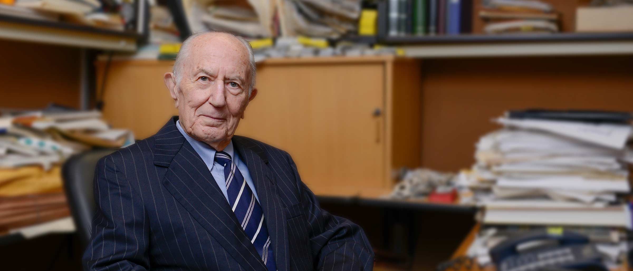 Older man in navy suit sitting at desk