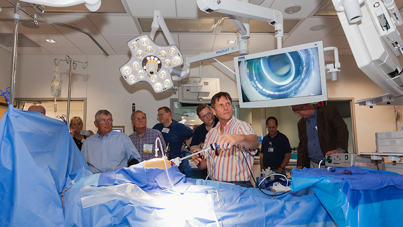 Group of people in a simulated operating room, one operating equipment while watching monitors