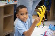 A student proudly displays his work in progress, a cut-out hand showing veins with colorful yarn.