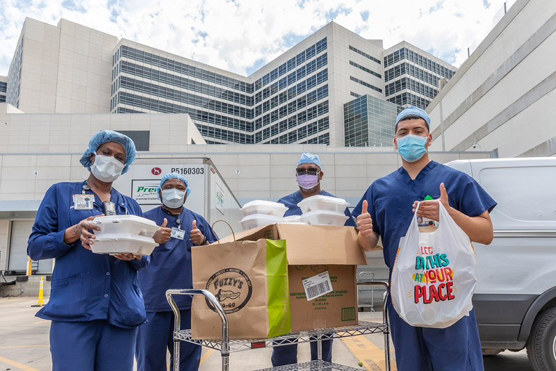 Medical works in scrubs and masks holding bags of tacos