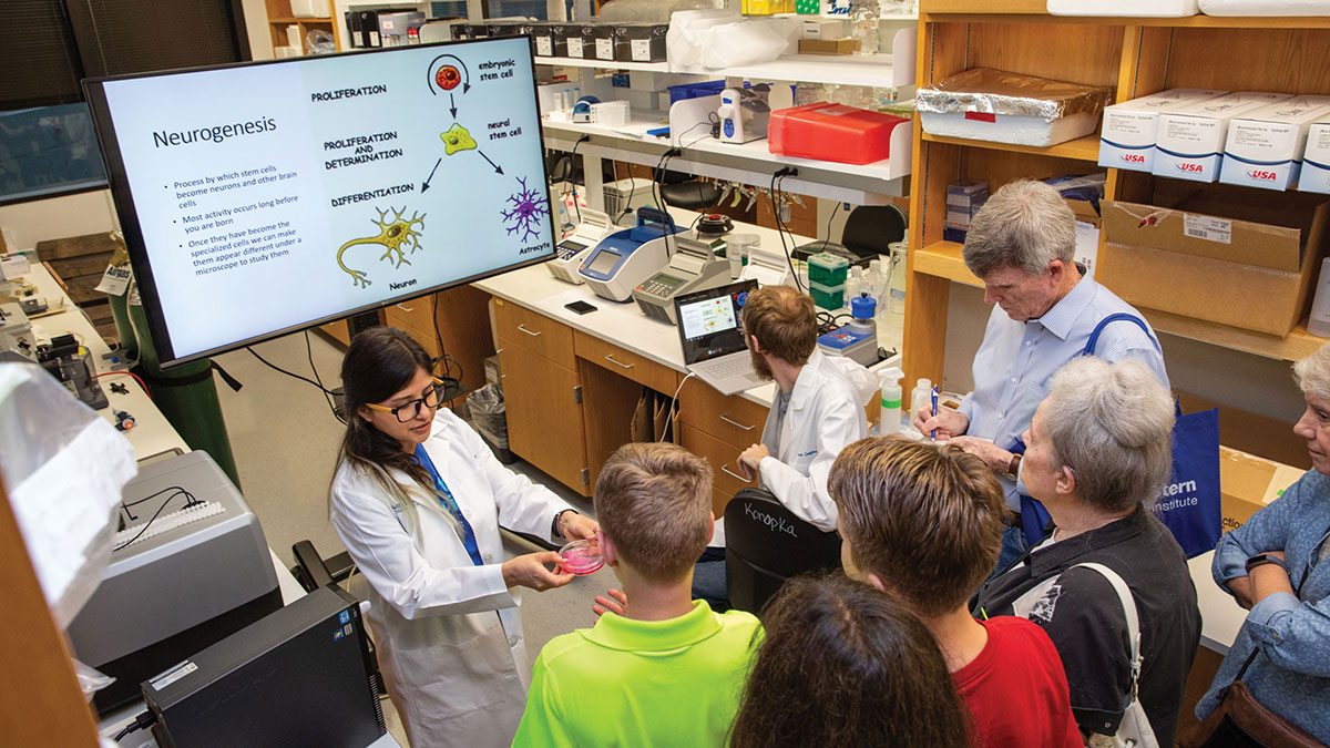 Graduate student Ana Ortiz and Research Technician Connor Douglas explain to visitors how brain cells are made.