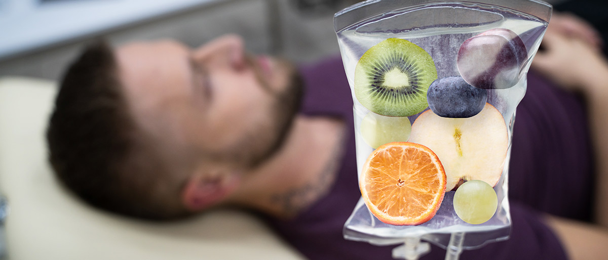 Man laying on back with IV filled with fruit in foreground