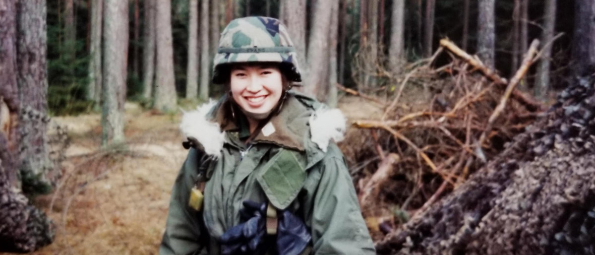 Woman in military fatigues, helmet, in woods