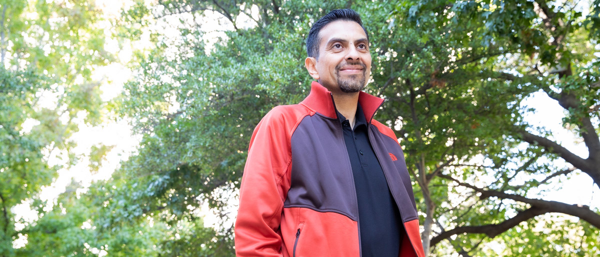 Man standing in red and black jacket in front of trees