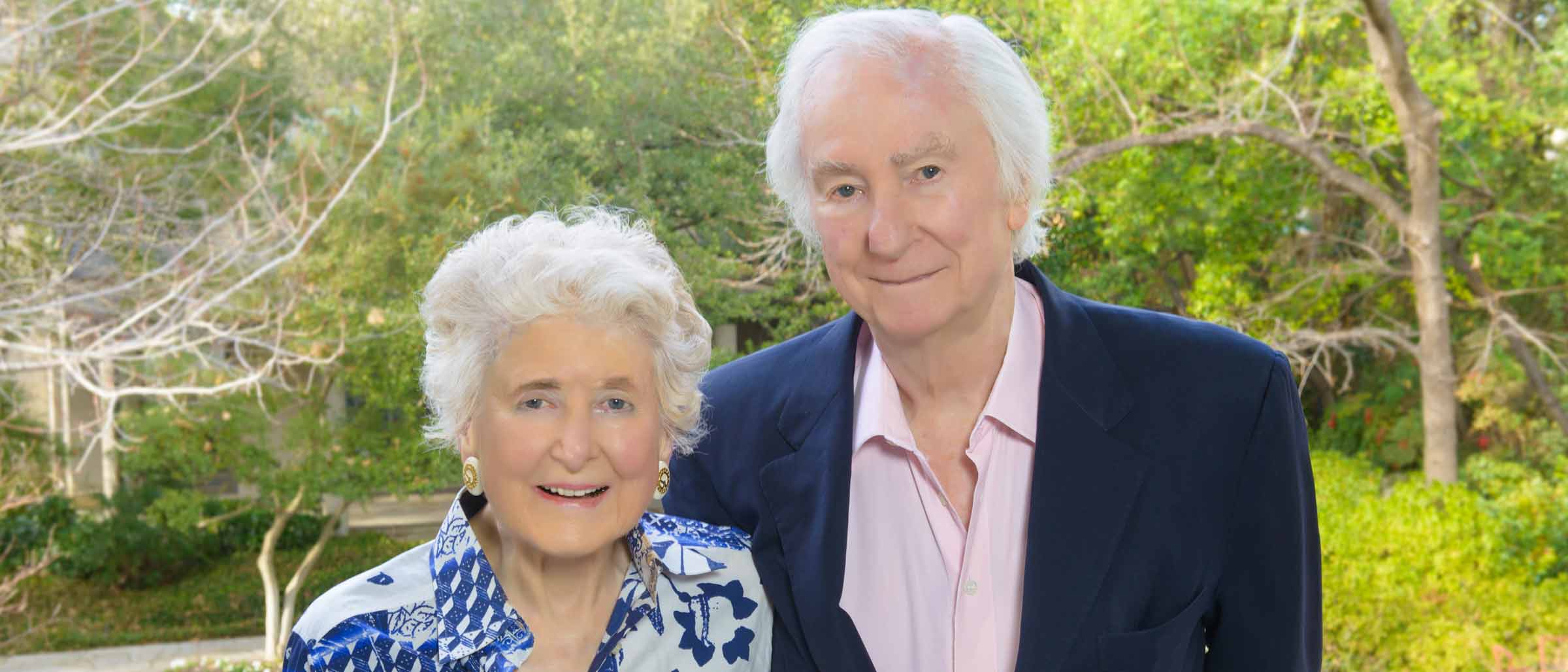 Older woman in blue patterned dress and man in blue suit, pink button down shirt.