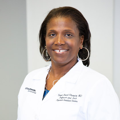 Woman with dark hair, hoop earrings, wearing white labcoat